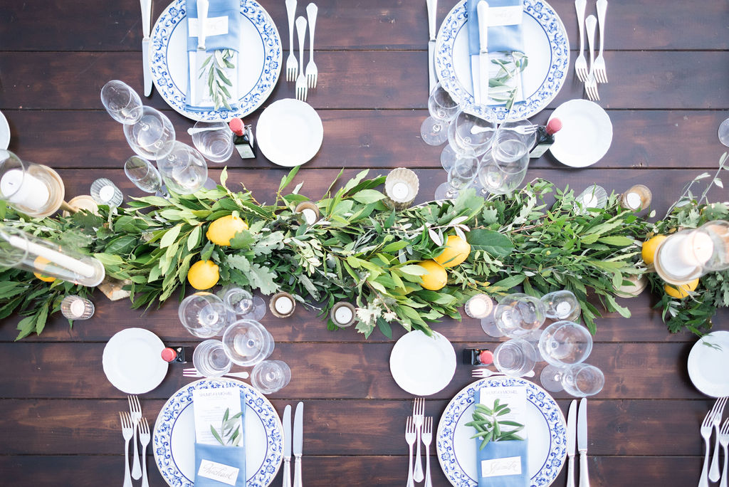 wooden table with greenery, lemons, tea lights and with and blue plates